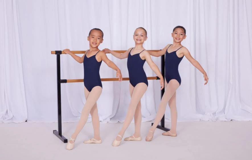 Three JMDS ballet students at the barre in navy leotards, pink tights and ballet shoes