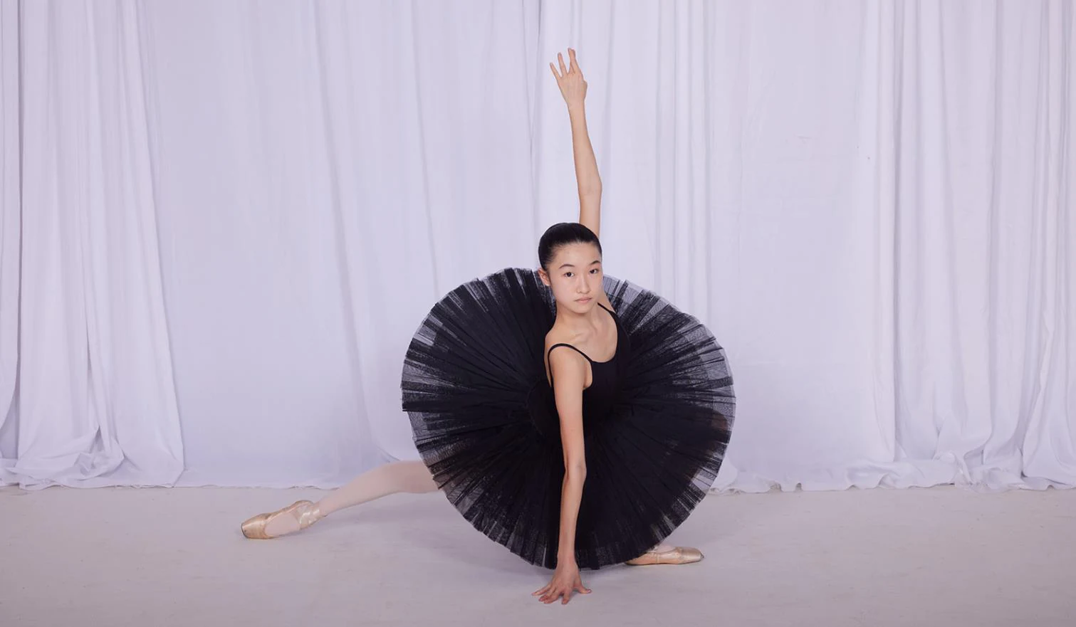 A JMDS ballet student in a black tutu and pointe shoes, in a deep lunge with one arm raised