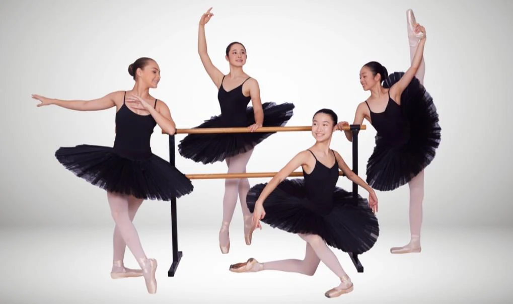 Four senior JMDS ballet students in black tutus posed around a barre